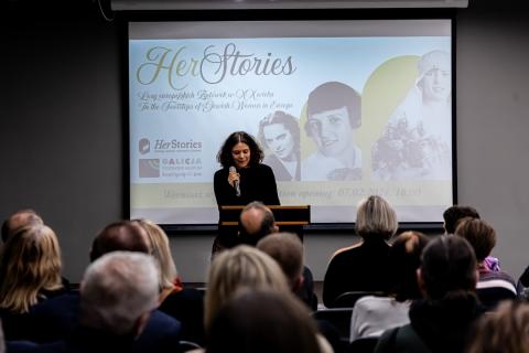 A conference room full of people. A woman - curator of the exhibition - is standing in front of them and speaking.